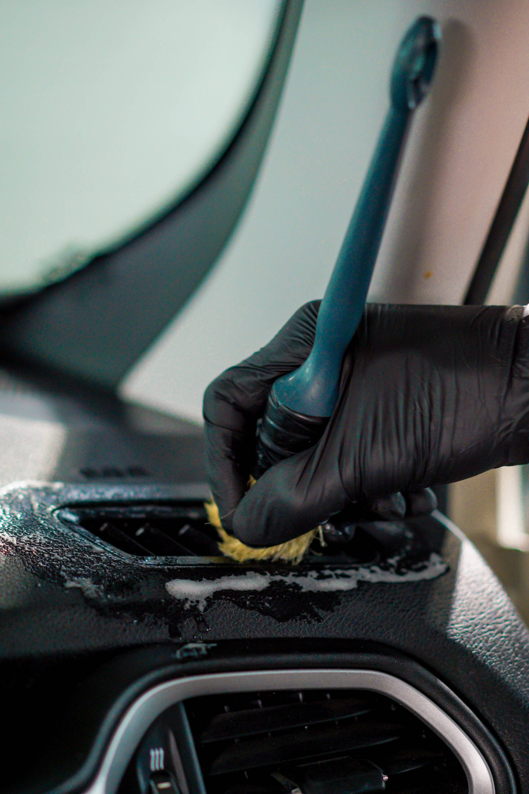 A close-up of a car wash worker using a brush and car chemicals to clean the dashboard of a luxury car during the detailing process