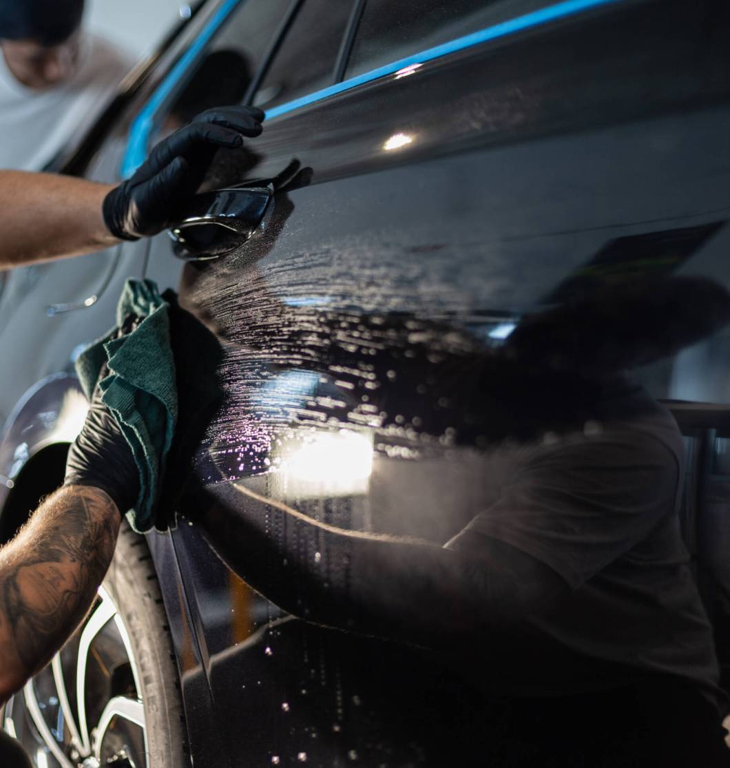 Man car washer washes car and wipes black car with rag in detail Man car washer washes car and wipes black car with rag in detailing studio
